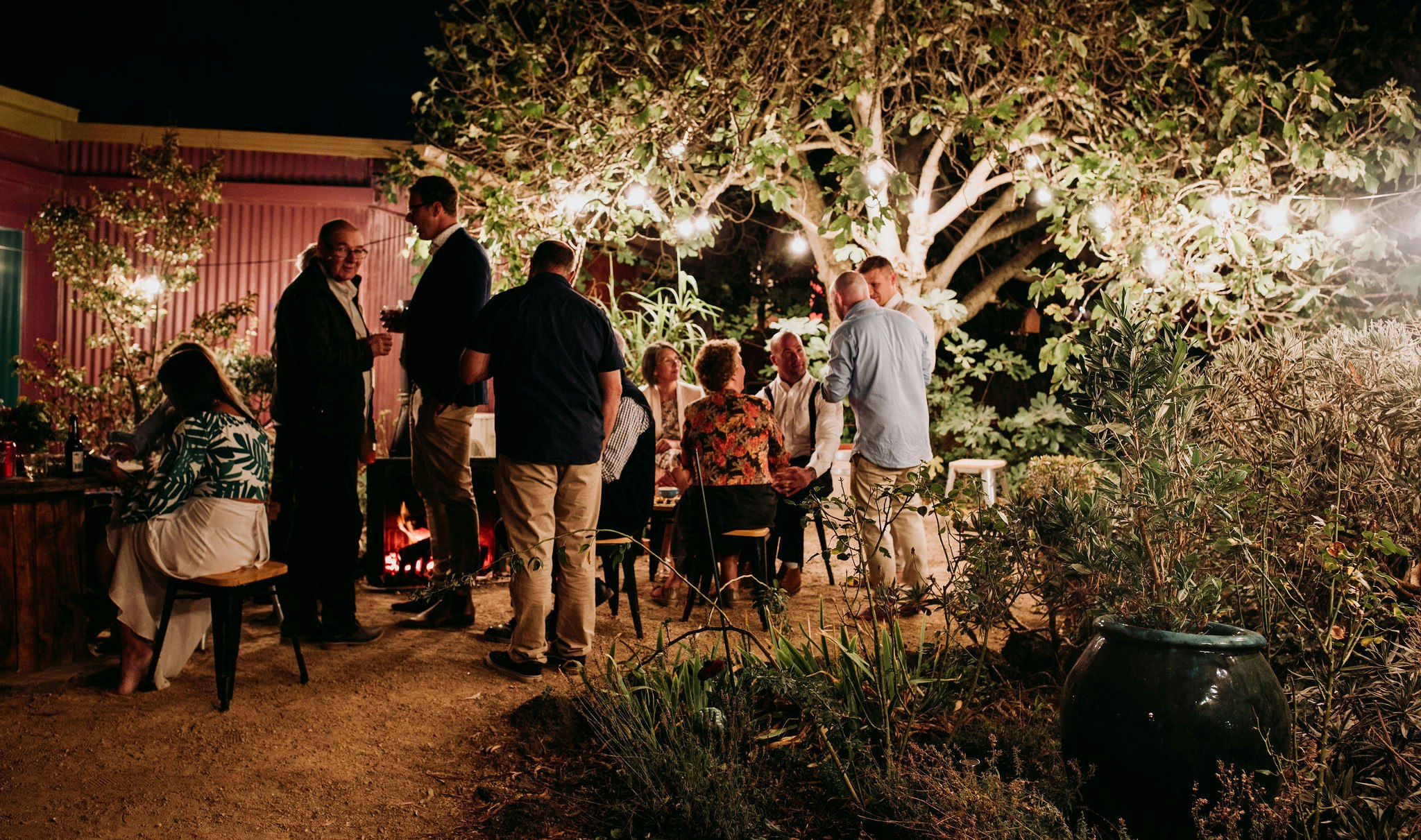 Wedding reception guests gathered under fairy lights at night.